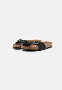 Black slides with a soft cork footbed, wide straps, and a silver adjustable buckle. The outsole features textured grip for traction.