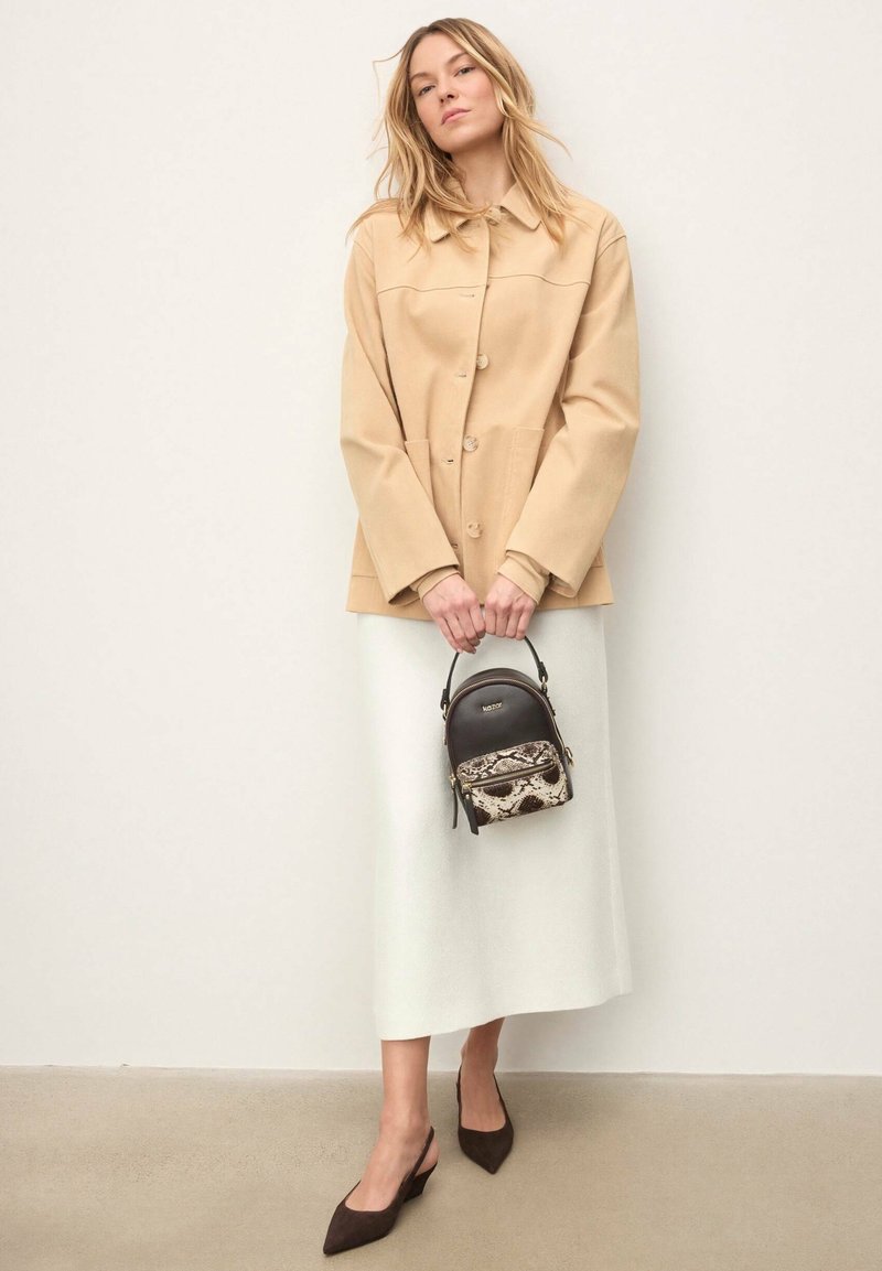 Béžová bunda na gombíky, krémová midi sukňa, hnedé semišové lodičky so zapínaním za pätou a malá čierna kabelka s hadím vzorom. Jednoduchý, čistý dizajn.
