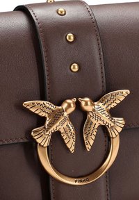Borsa a tracolla in pelle marrone con chiusura a forma di uccello in tonalità dorata, dettagli borchiati e cuciture, con un design strutturato e una texture liscia.
