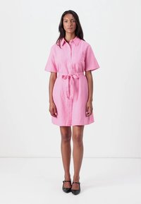 Kortermet rosa lin skjortekjole med knappestolpe, innsvingt midje med belte, og sidelommer. Jeg får en glatt tekstur og knelengde.