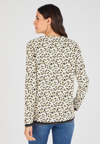 Top a maniche lunghe color crema con stampa leopardata nera e marrone, caratterizzato da un collo rotondo e un accento nero all'orlo.