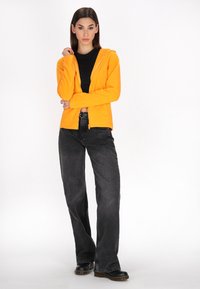 Felpa arancione con zip, top aderente nero, jeans neri larghi, scarpe nere con suola spessa. Tessuto liscio, design a gamba dritta, vestibilità casual.