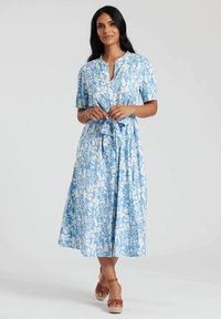 Niebieska sukienka w kwiaty z krótkimi rękawami, zapięciem na guziki przy dekolcie oraz przewiązywanym pasem. Materiał ma biały wzór roślinny i gładką fakturę.