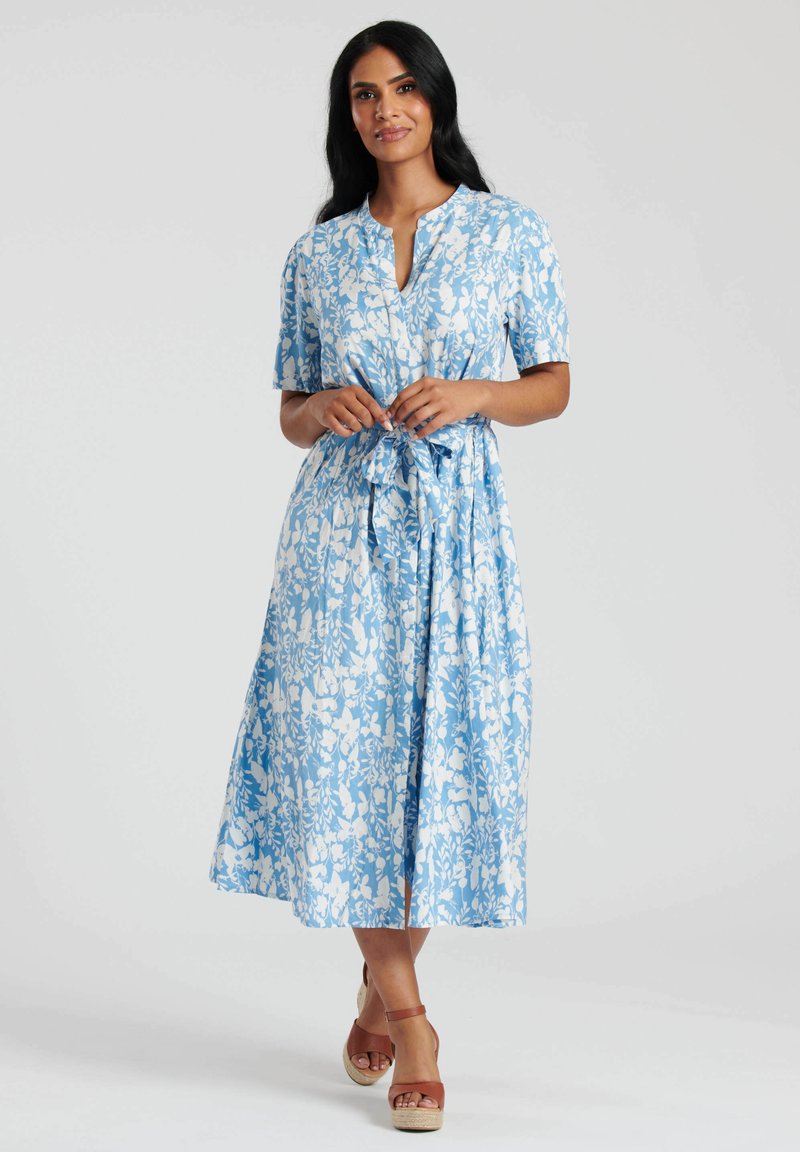 Niebieska sukienka w kwiaty z krótkimi rękawami, zapięciem na guziki przy dekolcie oraz przewiązywanym pasem. Materiał ma biały wzór roślinny i gładką fakturę.