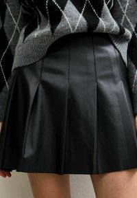 Schwarze, plissierte Lederrock mit glatter Textur. Kombiniert mit einem grauen, gemusterten Pullover mit einem Rautenmuster.