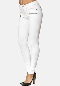 Jeans skinny bianchi con cerniere sulle tasche anteriori e dettagli in hardware dorato. Texture liscia, design aderente e dettagli di cucitura laterale.