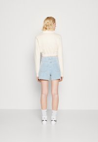 Cropped cream sweater and light blue denim shorts. The shorts have back pockets; paired with white socks and black-accented footwear.