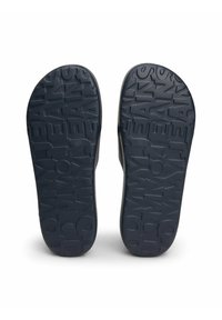 Suela de zapato de tela oscura azul con un diseño en relieve del logo "TOMMY JEANS". El material es goma con una superficie texturizada para mayor agarre.
