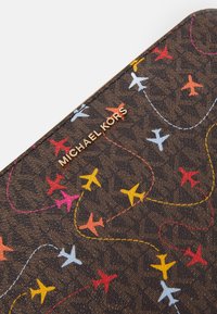 Portafoglio marrone a fantasia con motivi di aerei colorati in rosso, giallo, blu e rosa, con logo dorato "Michael Kors".