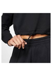 Svart croppad sweatshirt med elastisk nederkant och dragskojustering, i kombination med svarta byxor med elastisk midja. Slät tygtextur.