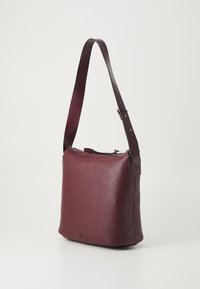 Burgunderfarget skinn crossover-veske med en teksturert overflate, justerbar stropp og glidelås på toppen. Firkantet form med minimalistiske designelementer.