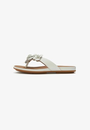 White flat sandal with thong strap and decorative flower detail on the wide front strap, brown sole, and cushioned footbed.