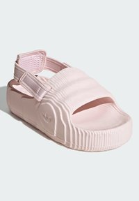 Ružové sandále s otvorenou špičkou, textúrovaným remienkom a nastaviteľným suchým zipsom. Majú hrubú, drážkovanú podrážku a vyrazené logo na boku.