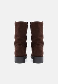 Bottines en suede marron avec un bout rond, une texture lisse et un petit talon noir. La vue arrière présente des plis doux et un minimalisme dans les détails.