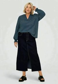 Blå, langermet bluse med v-hals; kombinert med en svart denim maxi-skjørt med en frontsliss og synlig søm; brukt med svarte sandaler.