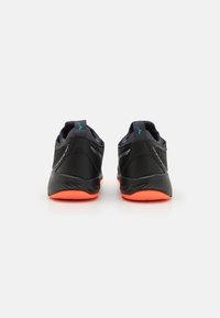 Schwarze Sportschuhe mit sleek Design, ausgestattet mit einer strukturierten Oberseite, reflektierenden Akzenten und leuchtend orangefarbenen Außensohlen.