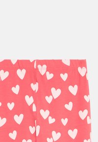 Κολάν από βαμβάκι με ελαστικότητα σε κοραλί ροζ απόχρωση, με διάσπαρτα λευκά σχέδια καρδιάς, διαθέτοντας ελαστική μέση και μαλακή υφή.