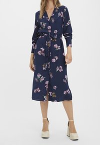Námořnické modré midi šaty s růžovým květinovým potiskem, knoflíková přední část, dlouhé rukávy, pásek v pase, nošeno s b�éžovými lodičkami na vysokém podpatku.