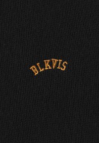 Czarna dziana czapka z teksturowanym wykończeniem. Posiada haftowane logo "BLKVLS" w kolorze pomarańczowym, łukowo umieszczone z przodu.