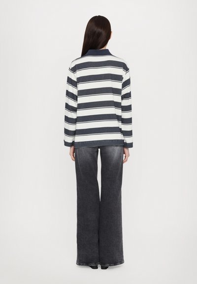 Langärmliges, gestreiftes Polohemd in Marineblau und Weiß mit Kragen, kombiniert mit weiten, dunklen Denim-Jeans. Mit aufgekrempelten Ärmeln.
