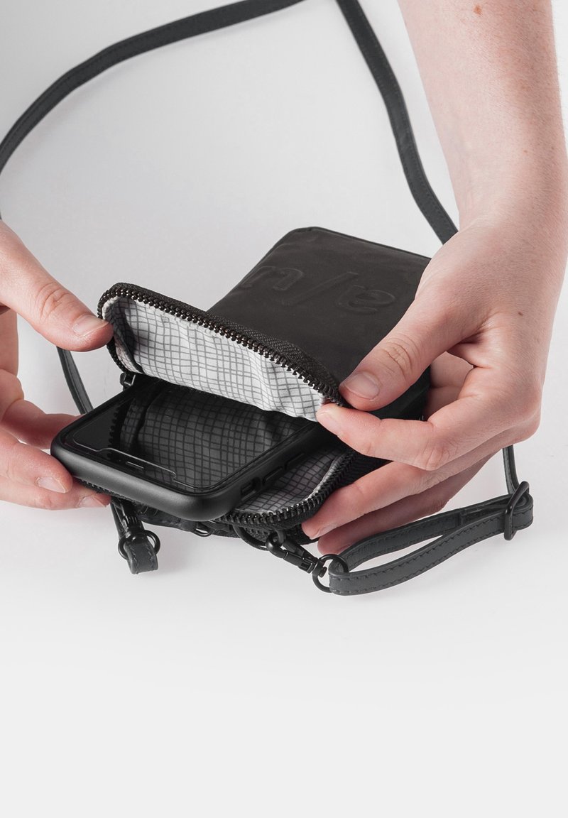 Schwarze Handy-Tasche mit Reißverschluss und grau gemustertem Innenfutter; wird von einer Hand gehalten, das Telefon ist sichtbar, mit einem abnehmbaren Riemen und strukturierten Akzenten.