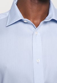 Světle modrá tkaná košile s límečkem na knoflíky a bíl�ými knoflíky, s texturovanou povrchovou úpravou.