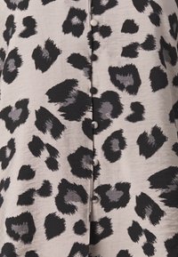 Blouse à imprimé léopard avec un tissu beige doux parsemé de taches noires et grises, fermeture à boutons et texture lisse.