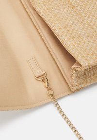 Sac en paille tressée avec une doublure en tissu beige. Il comprend un attachement en chaîne dorée et un fermoir. Design minimaliste avec une texture subtile.