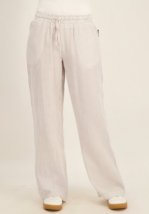 Loszittende broek met dunne verticale beige en witte strepen, elastische tailleband met trekkoord, gedragen met witte schoenen met rubberen zolen.