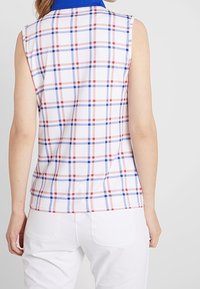 Ärmlös skjorta med blå krage, med en vit bakgrund som har ett rutmönster i röd och blå färg. Tillverkad av lättviktsmaterial.