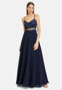 Robe de soirée bleu marine avec un corsage ajusté en sequins, une taille en dentelle transparente et une jupe fluide. Bretelles réglables et détail de fente sur le côté.