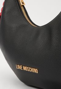 Black textured leather shoulder bag with a gold zip and logo. Rounded shape with a soft appearance, featuring a stitched finish and visible hardware.