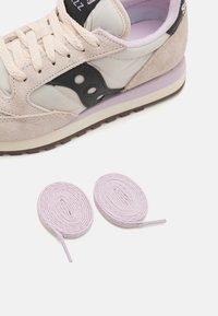 Sneaker v béžovej koži a semiši so sivým akcentom, s gumovou podrážkou a dvoma fialovými okrúhlymi šnúrkami. Tvary sú aerodynamické a funkčné.