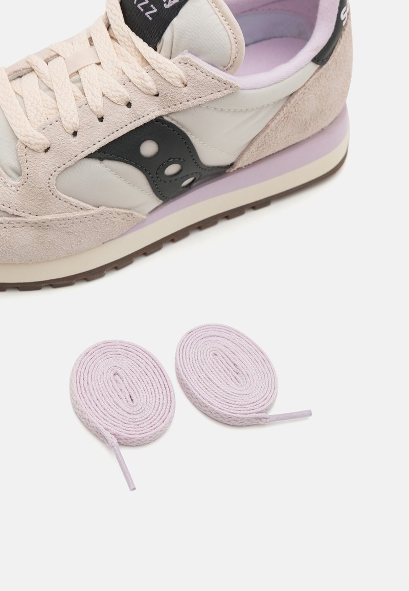 Sneaker in pelle beige e suede con un accento grigio, dotata di suola in gomma e due lacci rotondi lilla. Le forme sono streamline e funzionali.