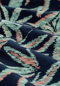 Tela de navy con un patrón texturizado que presenta remolinos en verde menta y coral, reminiscentes de hojas. Material suave y tejido con variaciones en el grosor de las líneas.