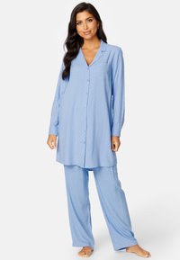 Jasnoniebieski zestaw piżamowy w kropki, składający się z koszuli zapinanej na guziki oraz luźnych spodni. Miękka tkanina i długie rękawy.