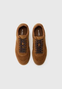 Brown suede sneakers with dark brown laces, round toe, and a cushioned interior. Features a smooth toe cap and stitching accents.