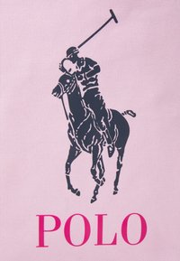 Silueta de jugador de polo montado en un caballo, balanceando un taco sobre su cabeza, sobre un fondo texturizado rosa con "POLO" en letras grandes de color rosa debajo.