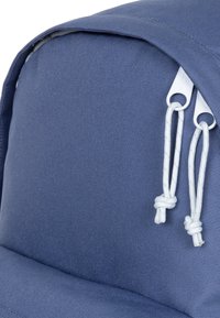 Modrý látkový batoh s hladkým povrchem, s kulatou horní částí, bílými zipovými stahováky a uzlovými bílými šňůrkami.