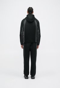 Czarny strój sportowy z kapturem, wyposażony w szare akcenty. Gładka tekstura, elegancki design i zwężane spodnie z zamkami przy kostkach.