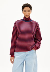 Langarm turtleneck in marineblauw en rode strepen, met een ontspannen pasvorm en zachte katoen. Gecombineerd met lichte wijde jeans.