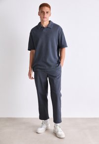 Mørk grå polo skjorte med krage, korte ermer og avslappet passform, parret med mørk grå avsmalnende bukser og hvite joggesko.