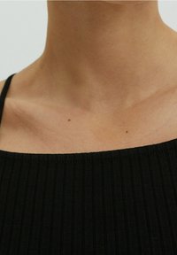 Primo piano della zona del collo e della clavicola di una persona che indossa una canotta nera a coste con spalline sottili.