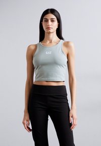Lys grønn avkortet tanktop med en tettsittende design; har en hvit "EA7" logo på brystet. Kombinert med svarte høyt midje leggings.