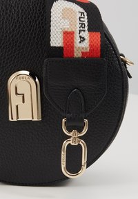 Borsa circolare in pelle nera con hardware dorato, caratterizzata da un logo Furla prominente e una tracolla colorata intrecciata con motivi audaci.