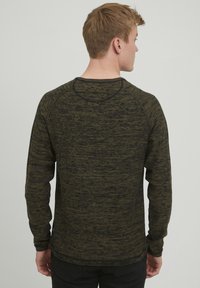 Langermet genser med rund hals i mørkegrønn og svart melert strikket stoff. Har ribbestrikket hals og mansjetter med raglanermer for bevegelse.