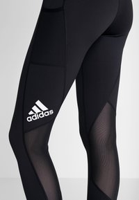 Svarta atletiska leggings med mesh-paneler och Adidas-logotyp. Funktioner en åtsittande design, elastiskt material och motsatta texturer.