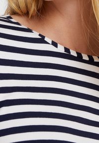 Laivastonsininen ja valkoinen raidallinen paita, joka on valmistettu pehmeästä kankaasta, jossa on leveä pääntie ja tasaisesti sijoitetut va horizontal pijat.
