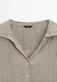 Beige linnen shirt met een gemêleerd, gekreukeld ontwerp, met een puntige kraag en drie knopen langs de knopenlijst.