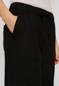 Pantalon de jogging noir avec une taille élastique, cordon de serrage et poches latérales. Le tissu a une texture lisse et un design décontracté.